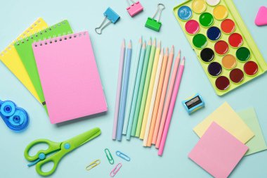 Okul malzemeleri renkli arka planda duruyordu. Not defterleri, kalemler, ataçlar ve makas. Düz görünüm.