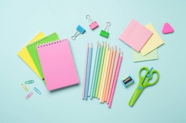 Malzemeler mavi arka planda yatıyordu. Not defterleri, kalemler, ataçlar ve makas. Düz görüntü. Pastel renklerde yaratıcı bileşim.