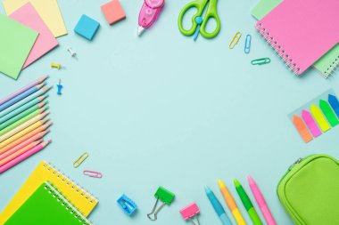 Malzemeler mavi arka planda yatıyordu. Not defterleri, kalemler, ataçlar ve makas. Düz görüntü. Tasarım için alanı olan çerçeve.
