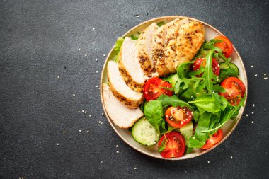 Siyah arka planda tavuk salatası. Izgara tavuk göğsü, domates ve yeşil yapraklar. Tasarım için alanı olan üst görünüm.