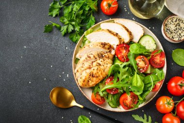 Siyah arka planda tavuk salatası. Izgara tavuk göğsü, domates ve yeşil yapraklar. Tasarım için alanı olan üst görünüm.