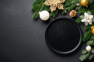 Noel sofrası. El işi tabağı, şarap kadehi, çatal bıçak takımı ve siyahta altın Noel süslemeleri. Kopyalama alanı olan düz.