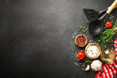 Mutfak masasında otlar, baharatlar ve mutfak aletleri var. Siyah arkaplanda üst görünüm.