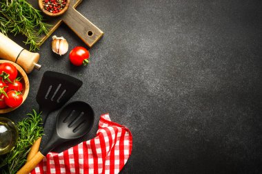 Food background. Kitchen utensils, wooden cutting board and food ingredients on black. Top view with copy space.