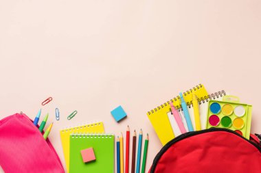 Okula dönelim. Okul çantası, renkli arka planda farklı kırtasiye malzemesi olan kalem kutusu. Kopyalama alanı olan düz.