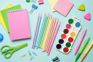 Mavi arka planda okul malzemeleri. Not defterleri, kalemler, suluboya resimler, okul ve sanat için kalemler. Düz yatıyordu.