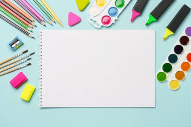 Çizim defteri, kalemler, suluboya boyalar ve mavi arka planda kalemler. Metin için alanı olan sanat yaratıcı bileşimi.