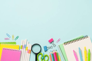 Okul gereçleri ya da mavi arka planda ofis kağıtları. Not defteri, kalemler, kalemler ve diğerleri. Metin için boşluk olan üst görünüm.