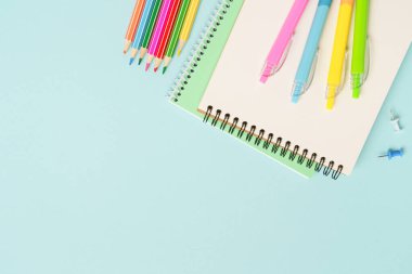 Not defteri, kalemler ve mavi arka planda renkli kalemler. Metin için boşluk olan üst görünüm.