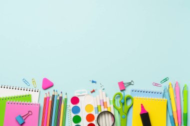 Okul gereçleri ya da mavi arka planda ofis kağıtları. Not defteri, kalemler, kalemler ve diğerleri. Metin için boşluk olan üst görünüm.