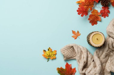 Samimi düşüşün arka planı düzdü. Örgü süveter, dökülen yapraklar ve mavi arka planda el yapımı mum..