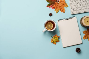 Sonbahar çalışma alanı düz arka planda yatıyordu. Dizüstü bilgisayar, defter, bardak çay ve dökülen yapraklar..