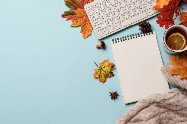 Sonbahar çalışma alanı düz arka planda yatıyordu. Dizüstü bilgisayar, defter, çay kupası, mavi arka planda örülmüş süveter..