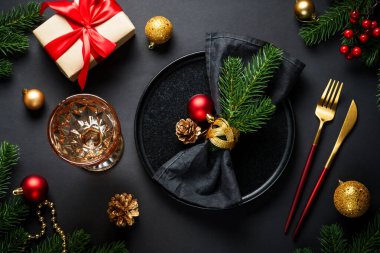 Siyah arka planda Noel yemeği. Noel sofrasında tabak, şarap kadehi, altın çatal bıçak takımı ve bayram süslemeleri..