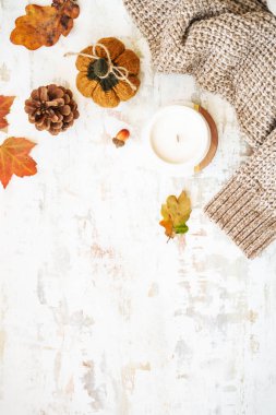 Beyazların rahat sonbahar arkaplanı. Sıcak kazak, sonbahar yaprakları, mum ve dekor. Kopyalama alanı olan düz resim.