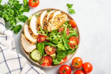 Izgara tavuk göğsü ve beyaz mutfak masasında taze sebzeli tavuk salatası. Üst görünüm.