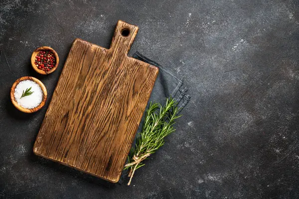 Kesme tahtası, baharatlar ve siyah arka planda bitkiler. Metin için boşluk ile düz uzandı.