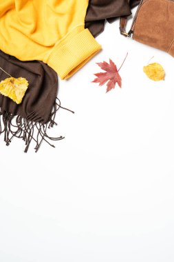 Sonbahar kumaşı ve aksesuarları beyaz arka planda. Atkı, kazak ve yapraklı çanta. Kopyalama alanı olan düz, dikey.