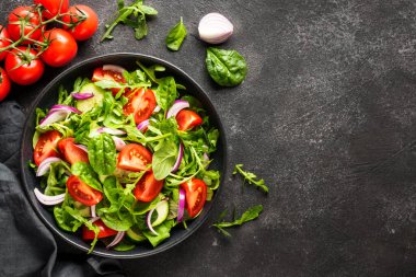 Yeşil yapraklı ve sebzeli taze salata. İçindekilerle birlikte siyah üzerine üstten görünüm.
