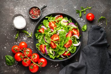 Yeşil yapraklı ve sebzeli taze salata. İçindekilerle birlikte siyah üzerine üstten görünüm.