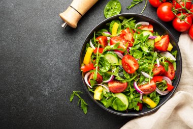 Yeşil yapraklı ve sebzeli taze salata. İçindekilerle birlikte siyah üzerine üstten görünüm.