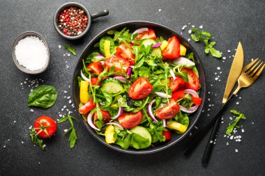Yeşil yapraklı ve sebzeli taze salata. İçindekilerle birlikte siyah üzerine üstten görünüm.