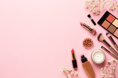 Makyaj ürünleri ve çiçekler pembe arka planda. Göz farı, fosforlu kalem, krem, ruj ve kozmetik fırçalar..