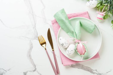 Bahar masası, beyaz tabak, altın çatal bıçak takımı ve renkli paskalya yumurtaları. Kopyalama alanı olan üst görünüm.