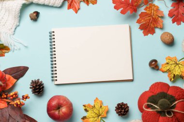 Şükran Günü geçmişi. Düşen yapraklar, not defteri, örgü eşarp ve mavi arka planda ahşap mum..