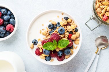 Beyaz masada taze böğürtlenli yoğurt ve tahıl gevreği. Sağlıklı atıştırmalıklar ya da kahvaltı. Beyaz arkaplanda kopyalama alanı olan üst görünüm.