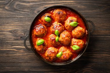 Ahşap masada fesleğen yapraklı domates soslu köfte. Üst görünüm.