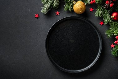 Noel sofrası. Noel yemeği. Siyah arka planda siyah tabaklar, çatal bıçak takımı ve süslemeler. Kopyalama alanı olan düz.