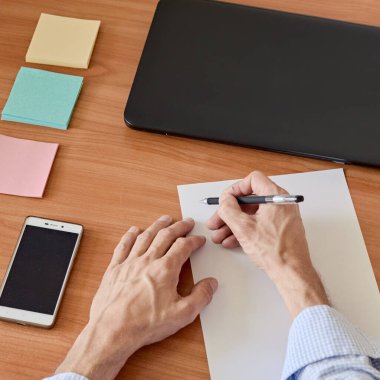 Dizüstü bilgisayar, akıllı telefon, bir fincan kahve ve kağıt üzerine erkek el yazısı.