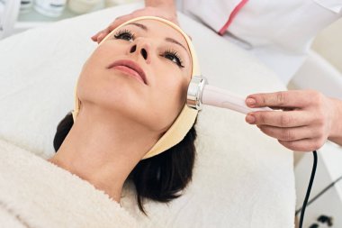 Closeup photo of professional beautician doing facial mesotherapy to young woman