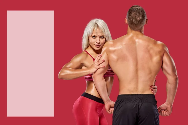 Fit strong muscular bodybuilding couple posing together on red background with copyspace