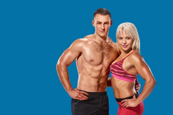 Beautiful couple of muscular fit man and woman bodybuilder hugging on azure shade blue background