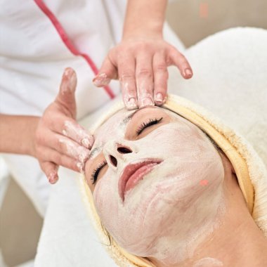 Yüzünde krem olan genç bir kadın yüz masajı yaptırıyor.