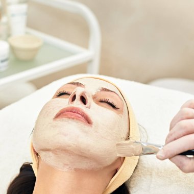 Cosmetologist applying peeling mask on face of her female client