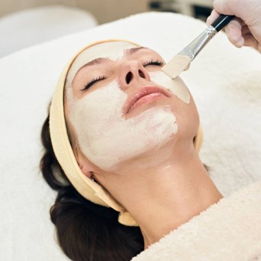 Cosmetologist applying peeling mask on face of her female client