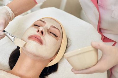 Cosmetologist applying peeling mask on face of her female client