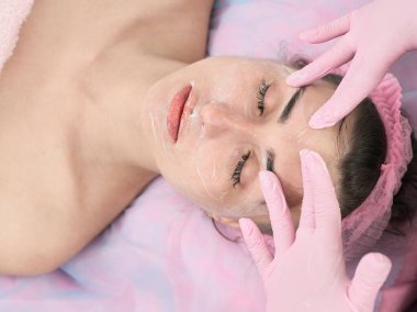 Kozmetik uzmanı, genç bir kadının yüzünü soymak için ameliyata hazırlanıyor.