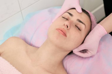 Kapalı gözlerle uzanan ve kaplıcada kafa masajı yaptıran genç bir kadın.