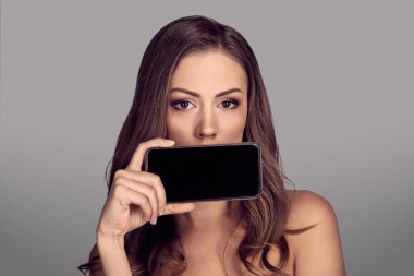 Güzel, çıplak bir kadının modern akıllı telefonuyla ağzını kapattığı portresi.