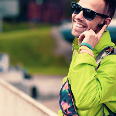 Gülümseyen mutlu turist bluetooth kulaklık cihazıyla telefonda konuşuyor.