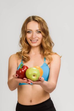 Elinde meyve ve sebzelerle gülümseyen sporcu kadının portresi.