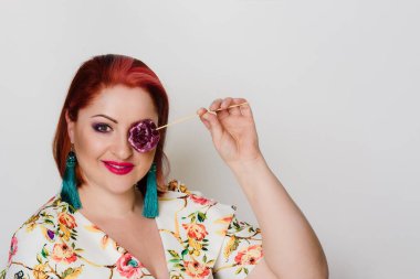 Gülümseyen kızıl saçlı kadının portresi lolipopla poz veriyor.