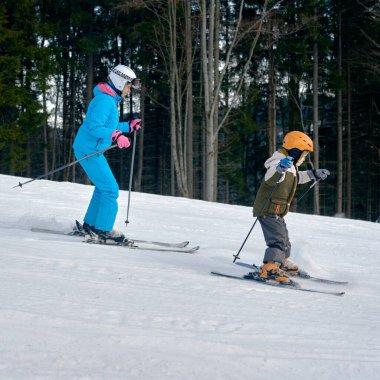 Genç bir çocuk ve annesi dağlarda kayak tatilinin keyfini çıkarıyorlar.
