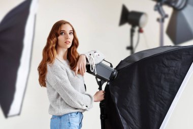 Modern fotoğraf stüdyosunda çalışan genç ve güzel yaratıcı kadın fotoğrafçının portresi, iş meraklısı bir kadın, ışık ve kameralı bir stüdyoda fotoğraf ekipmanları sergiliyor..