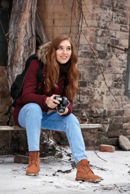 Kış şehrinde bankta kameralı mutlu ve çekici bir kızıl kız oturuyor.