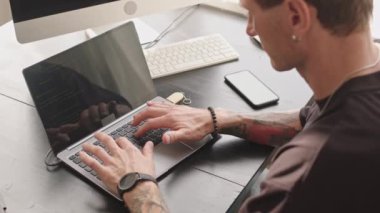 Yukarıdan, yazılım geliştirme programında program koduyla çalışan yavaş dövmeli Kafkasyalı adamla yakın çekim.
